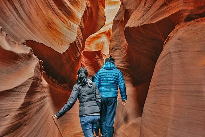 Two visitors walking through a narrow Antelope Canyon passage